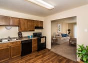 Thumbnail 3 of 10 - Grand Forks, ND Stanford Court Apartments. A kitchen with black appliances and a living room in the background