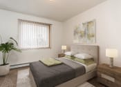 Thumbnail 4 of 10 - Grand Forks, ND Vista Apartments. A bedroom with a bed, night stand, and a plant in the corner next to the window.