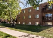 Thumbnail 15 of 16 - Grand Forks, ND Mayfair Apartments. An exterior of a three level apartment building with a sidewalk out front.