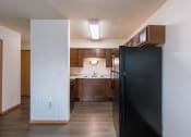 Thumbnail 11 of 16 - an empty kitchen with a black refrigerator and wooden cabinets. Moorhead, MN South Park Apartments