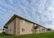 Thumbnail 1 of 11 - an apartment building with a cloudy sky in the background. Moorhead, MN Woodstone Apartments