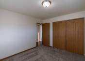 Thumbnail 14 of 16 - an empty living room with a carpeted floor and two wooden doors. Fargo, ND North Manor Apartments