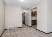 Thumbnail 19 of 23 - Omaha, NE Maple Ridge Apartments. A living room with a carpeted floor and a kitchen in the background