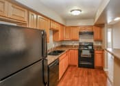 Thumbnail 17 of 34 - a kitchen with wooden cabinets and appliances and a black refrigerator. Omaha, NE Evergreen Terrace Apartments