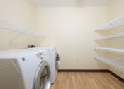 Thumbnail 9 of 21 - a laundry room with a washer and dryer and shelves. Fargo, ND Crossroads Apartments