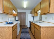 Thumbnail 8 of 20 - a kitchen with wood cabinets and white appliances and a blue rug. Fargo, ND Park Circle Apartments.