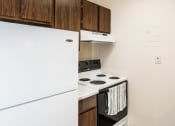 Thumbnail 7 of 23 - Grand Forks, ND Riverwood Apartments. A kitchen with white appliances and wooden cabinets and a refrigerator