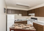 Thumbnail 13 of 23 - Grand Forks, ND Riverwood Apartments. A kitchen with white appliances and brown cabinets and granite counter tops