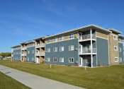 Thumbnail 17 of 18 - an exterior view of an apartment building with a green lawn. Moorhead, MN Sandy Creek Apartments