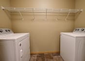Thumbnail 37 of 45 - two washers and a dryer in a laundry room with a rack on top. Fargo, ND Urban Plains Apartments
