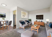 Thumbnail 2 of 23 - A living room with a grey couch, a wooden coffee table, and a painting on the wall.