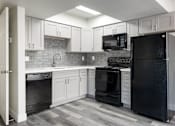 Thumbnail 7 of 23 - A black refrigerator stands in a kitchen with white cabinets and a black oven.