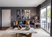 Thumbnail 5 of 31 - A modern living room with a grey couch, a large abstract painting, and a marble coffee table.