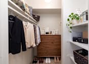 Thumbnail 31 of 31 - A small closet with a wooden dresser and clothes hanging on a rail.