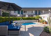 Thumbnail 32 of 34 - A poolside patio with a black umbrella and blue cushioned furniture.