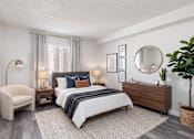 Thumbnail 14 of 34 - A bedroom with a large bed, a chair, a side table with lamps, a dresser, and a potted plant.
