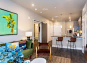 Thumbnail 2 of 29 - A living room with a green couch and a painting of yellow flowers on the wall.
