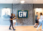 Thumbnail 10 of 29 - People walking in front of a wall with a GW sign on it.