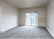 Thumbnail 4 of 17 - A large empty room with a carpeted floor and a sliding glass door leading to a balcony at Courtyard Apartments on Belsly  Apartments, Moorhead, MN