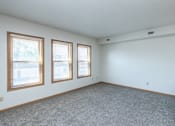 Thumbnail 10 of 16 - A room with a grey carpet and three windows, Kassenborg Apartments, Moorhead, MN