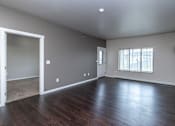 Thumbnail 6 of 10 - A large empty room with wood flooring and a window with blinds.