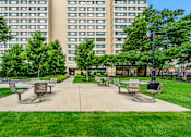 Thumbnail 12 of 13 - A park with a grassy area and benches in front of a large building.