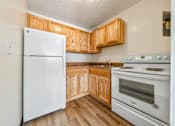 Thumbnail 7 of 13 - A white refrigerator stands in a kitchen with wooden cabinets and a white oven at 500 Manila Senior Apartments in Jersey City