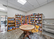 Thumbnail 16 of 25 - a library with a table and chairs and shelves of books