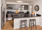 Thumbnail 1 of 19 - Kitchen with dark cabinets, quartz counters, and a peninsula with two chairs behind it.