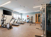 Thumbnail 44 of 49 - A spacious gym with a variety of equipment including treadmills, elliptical machines, and a weight machine.