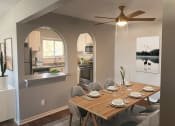 Thumbnail 2 of 17 - Dining nook with view into the kitchen area, with table, art, overhead fan and lighting, with grey walls and darker plank flooring. Updated finishes and stainless steel apliances