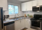 Thumbnail 3 of 17 - Cedarvale Elite one bedroom kitchen with stainless steel microwave, oven, dishwasher, and fridge, with elegant white cabinetry. 