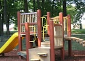 Thumbnail 23 of 23 - A playground with a yellow slide and a wooden structure at Potomac Ridge Apartments, Woodbridge, Virginia