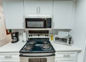 Thumbnail 15 of 36 - a kitchen with a stove top oven next to a microwave at Juniper Springs Apartments, Austin, TX