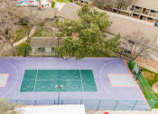 Thumbnail 7 of 36 - an aerial view of a tennis court and a house on a blue and green court at Juniper Springs Apartments, Austin, TX
