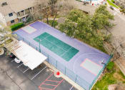Thumbnail 9 of 36 - an aerial view of a tennis court and a basketball court with trees at Juniper Springs Apartments, Austin, TX