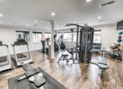 Thumbnail 23 of 36 - a gym with cardio equipment and weights on a wooden floor at Juniper Springs Apartments, Austin, TX