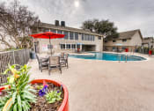 Thumbnail 10 of 36 - a backyard with a pool and patio with tables and umbrellas at Juniper Springs Apartments, Austin, TX