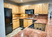 Thumbnail 14 of 37 - a kitchen with wooden cabinets and a black refrigerator at Le Montreaux Apartments, Austin, TX, 78759