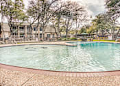 Thumbnail 4 of 37 - Swimming pool with brick decking and tree canopy at Le Montreaux Apartments, Austin, TX 78759
