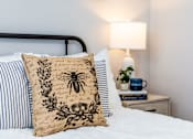 Thumbnail 9 of 17 - A bed with a bee design on the pillow and a lamp on the side table.