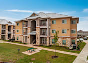 Thumbnail 4 of 16 - Apartment complex with a green lawn and a tree in front.
