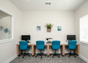 Thumbnail 9 of 9 - A room with a white wall and a window with blinds, has a desk with four chairs and a plant on it.