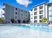 Thumbnail 4 of 9 - A large swimming pool in front of a multi-story residential building.