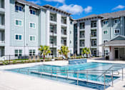 Thumbnail 2 of 9 - A swimming pool in front of a multi-story apartment building.