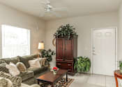 Thumbnail 6 of 12 - A living room with a couch, a coffee table, a plant, and a cabinet.