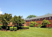 Thumbnail 11 of 39 - A grassy area in front of a building with trees and bushes.