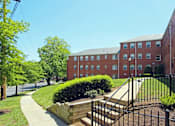 Thumbnail 10 of 39 - A red brick building with a black fence and a green lawn in front.
