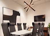 Thumbnail 11 of 25 - A conference room with a large table surrounded by chairs and a chandelier hanging from the ceiling at The Olivia Apartments, Carmel, IN, 46032