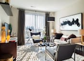 Thumbnail 7 of 25 - A living room with a grey couch, a black chair, and a large abstract painting on the wall at The Olivia Apartments, Carmel